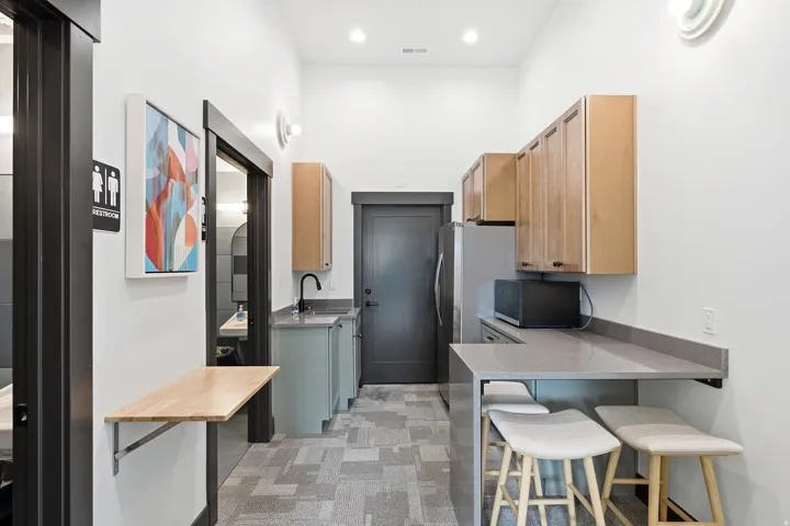 Compact kitchen with light wood-finish cabinetry, a black faucet, and a grey countertop extending to a breakfast bar