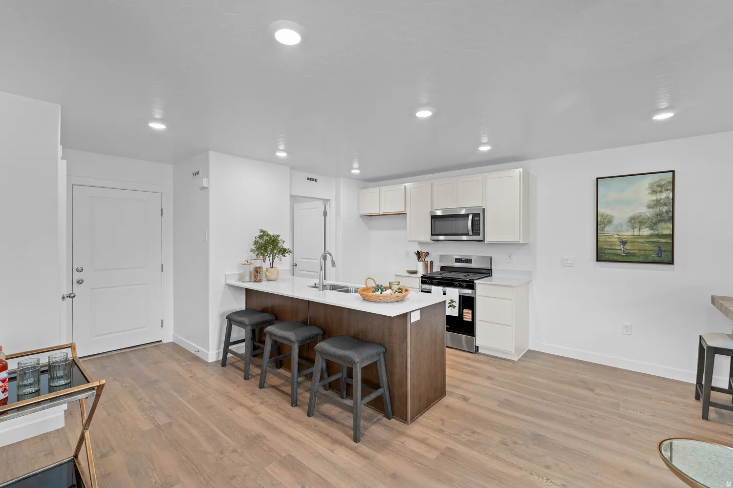 Modern kitchen featuring an island with white countertop, stainless steel appliances, white cabinetry, and wood-finish flooring