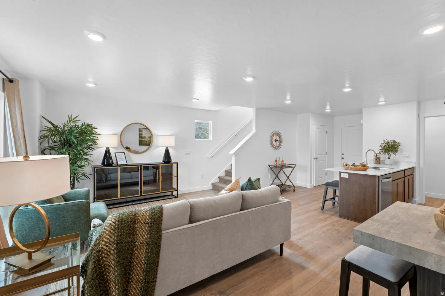 Bright, open-concept living area featuring wood-finish flooring, recessed lighting, a kitchen island with seating, and a staircase with a white railing