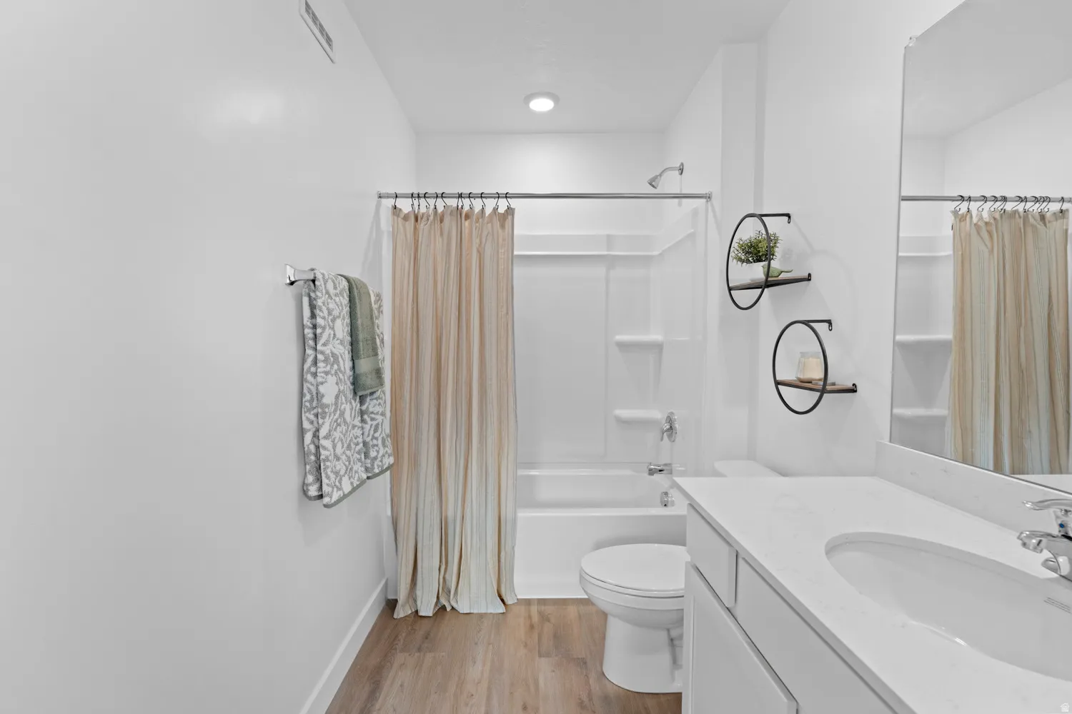 Bathroom featuring a white vanity with an integrated sink, a large wall-mounted mirror, and wood-finish flooring