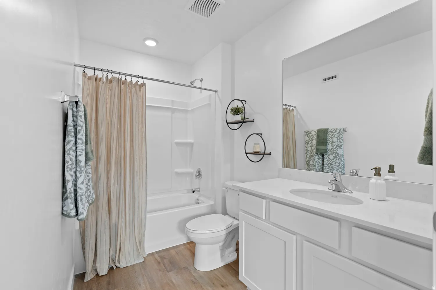Bathroom featuring a white bathtub/shower combination, a single vanity with an integrated sink, a large mirror, and wood-finish flooring