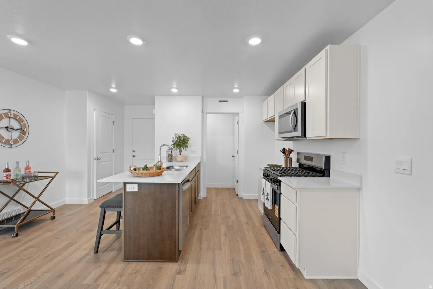 Modern kitchen featuring a central island with a sink, stainless steel appliances, white cabinetry, wood-finish flooring, and recessed lighting