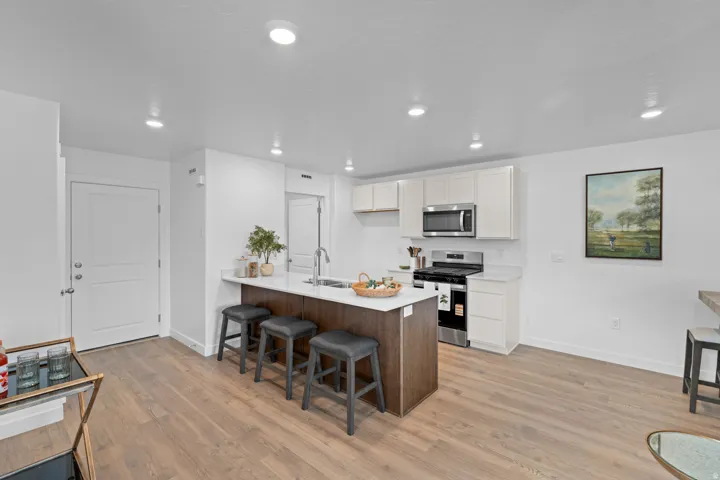 Modern kitchen featuring an island with white countertop, stainless steel appliances, white cabinetry, and wood-finish flooring