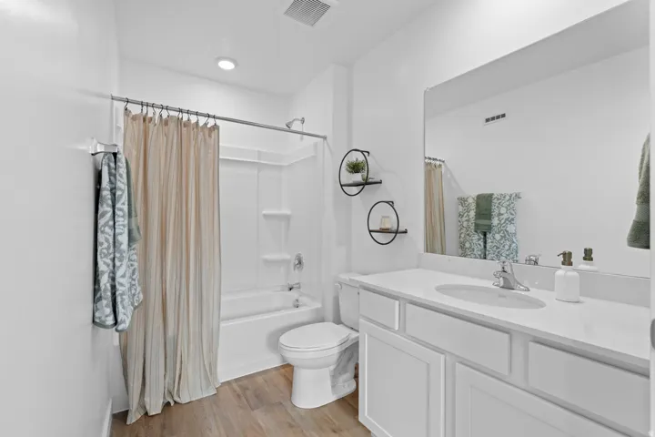 Bathroom featuring a white bathtub/shower combination, a single vanity with an integrated sink, a large mirror, and wood-finish flooring