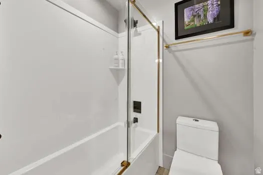 Contemporary bathroom featuring a white tub-shower combination with gold-finish hardware, clear glass shower enclosure, and a built-in shower shelf
