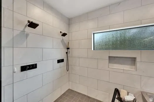 Shower enclosure featuring light-colored rectangular wall tile and a grey square-tiled floor