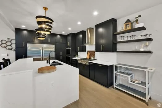 Gourmet kitchen featuring a large central island with an integrated sink, black cabinetry, professional-grade stainless steel appliances, a modern spiral pendant light fixture, and recessed lighting
