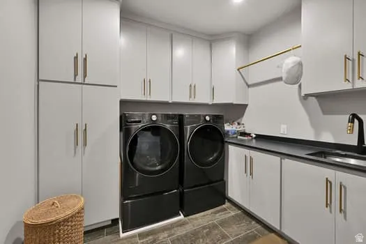 Dedicated laundry room featuring light gray cabinetry with gold-tone hardware, black countertop, and a stainless steel sink with a black and gold-tone faucet
