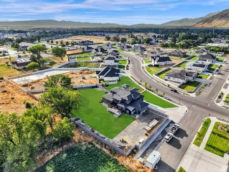 Aerial view of a contemporary residential community featuring a dark-toned property with a manicured lawn, established trees, and surrounding concrete hardscaping