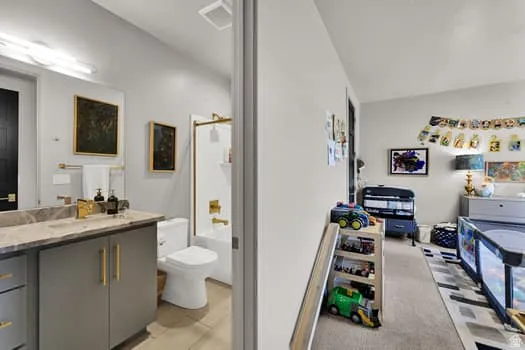 Bathroom featuring a single vanity with a stone-finish countertop, undermount sink, and gold-tone fixtures