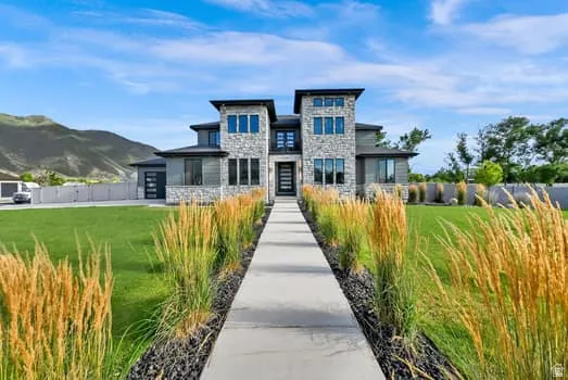 Contemporary exterior featuring stone accents, a concrete walkway, mature ornamental grasses, a manicured lawn, and a mountain backdrop