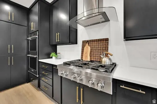 Modern kitchen featuring black cabinetry with gold-tone hardware, white countertops, a stainless steel gas range, and a coordinating stainless steel double wall oven