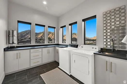 Utility room featuring abundant white cabinetry with gold-toned hardware, dark countertops, a built-in sink, and multiple windows showcasing mountain scenery