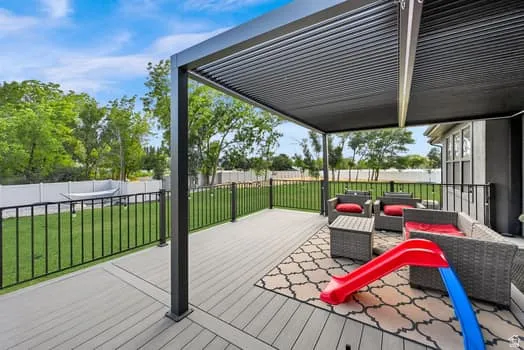 Spacious outdoor deck featuring a contemporary louvered pergola, composite decking, and black metal railings overlooking a manicured lawn