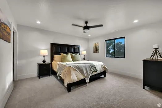 Recessed lighting illuminates this carpeted bedroom featuring a ceiling fan, a window with a black frame, and a dark wood headboard