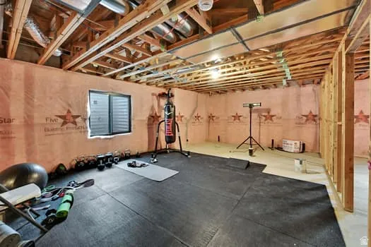Unfinished lower level with exposed ceiling joists and wall studs, offering an egress window and partial rubber flooring