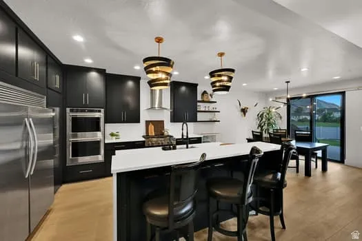 Modern kitchen featuring black cabinetry, stainless steel appliances, a white island countertop, and wood-finish flooring