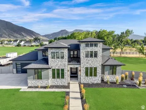 Contemporary stone and stucco residence with a multi-level design, featuring a prominent two-story entryway, multiple large windows, and a paved walkway leading to the entrance