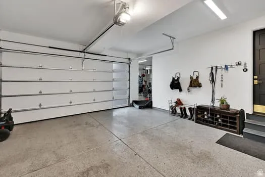 Attached garage featuring a white sectional door, concrete flooring, overhead lighting, and a dark-paneled entry door