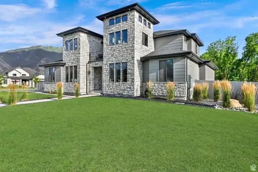Contemporary exterior featuring stone accents, horizontal siding, multiple large windows, and a landscaped front yard with a concrete pathway