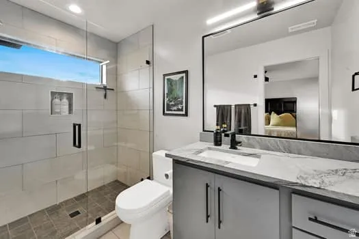 Modern bathroom featuring a frameless glass shower enclosure, a rectangular window, a built-in shower niche, a gray vanity cabinet with black hardware, and a single basin sink with a stone countertop