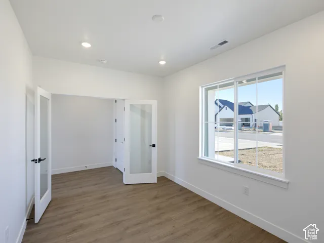 Neutral-toned interior featuring wood-finish flooring, recessed lighting, expansive dual-pane windows, and white-framed glass French doors with matte black hardware