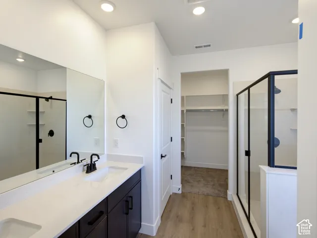 Bathroom featuring a dual-sink vanity with light-toned countertops, dark cabinetry, recessed lighting, walk-in shower with black-framed glass enclosure, and built-in closet shelving