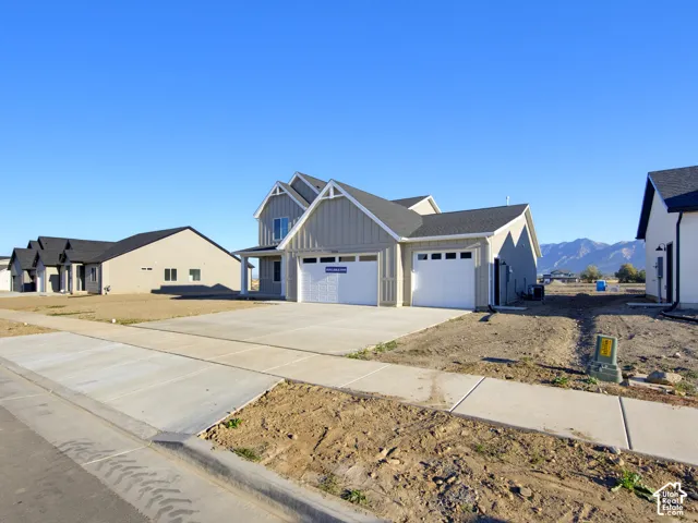 Two-story residence featuring vertical siding, a three-car garage with paneled doors, and asphalt shingle roofing, set against a mountain backdrop