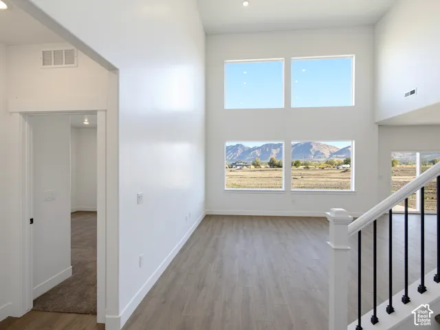 Double-height ceiling, large stacked windows, wood-finish flooring, mountain backdrop, and staircase with white railings and black metal balusters