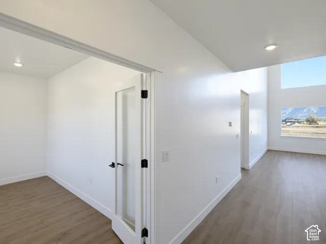 Wood-finish flooring, glass-panel interior door with matte black hardware, recessed ceiling lighting, high-ceiling wall segments, and large windows with mountain scenery