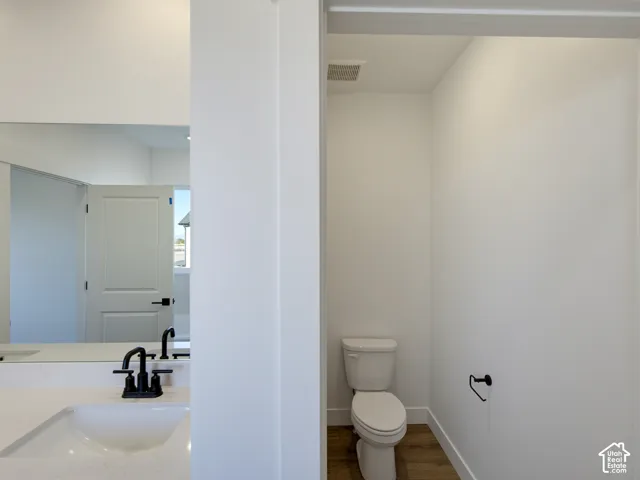 Bathroom featuring a vanity with a white countertop, undermount sink, and matte black plumbing fixtures, paired with wood-finish flooring and a wall-mounted toilet paper holder