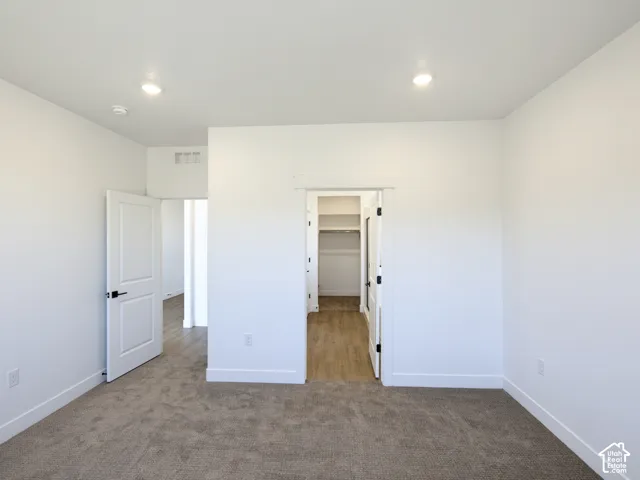 Neutral-toned carpeting, recessed ceiling lighting, two-panel interior doors with matte black hardware, and an accessible closet featuring integrated shelving