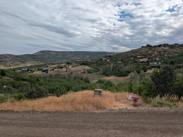 Expansive natural landscape featuring rolling hills, scattered trees, and distant residential structures
