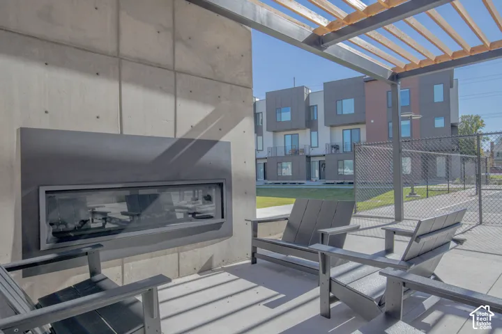 Outdoor patio featuring a concrete accent wall, linear built-in fireplace, and overhead wooden pergola