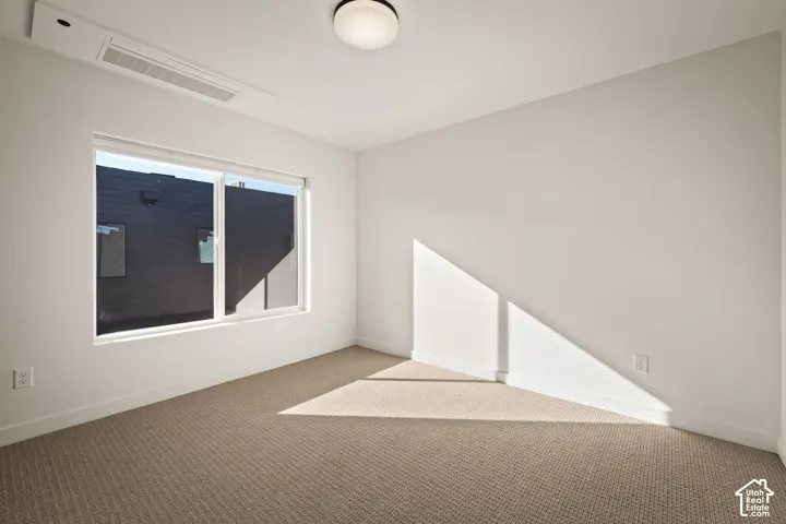 Neutral wall-to-wall carpeting, large window with a white frame, recessed ceiling light fixture, and integrated wall-mounted heating and cooling unit