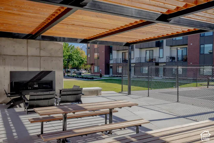 Outdoor patio featuring a cedar-plank pergola, exposed aggregate concrete flooring, an inset gas fireplace, and a built-in bench