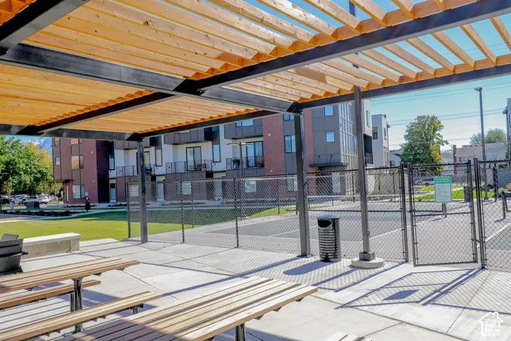 Outdoor recreation area featuring a metal and wood-slat pergola, paved concrete patio, and fenced-in court