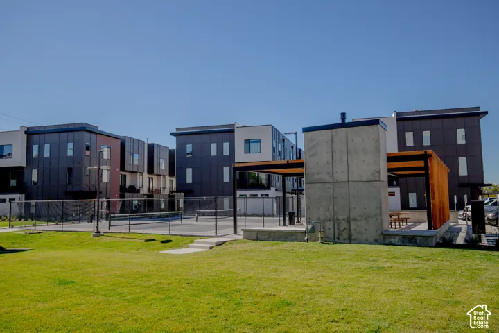 Outdoor recreational space featuring a fenced sports court, concrete-constructed pavilion, pergola-style structure, and manicured lawn