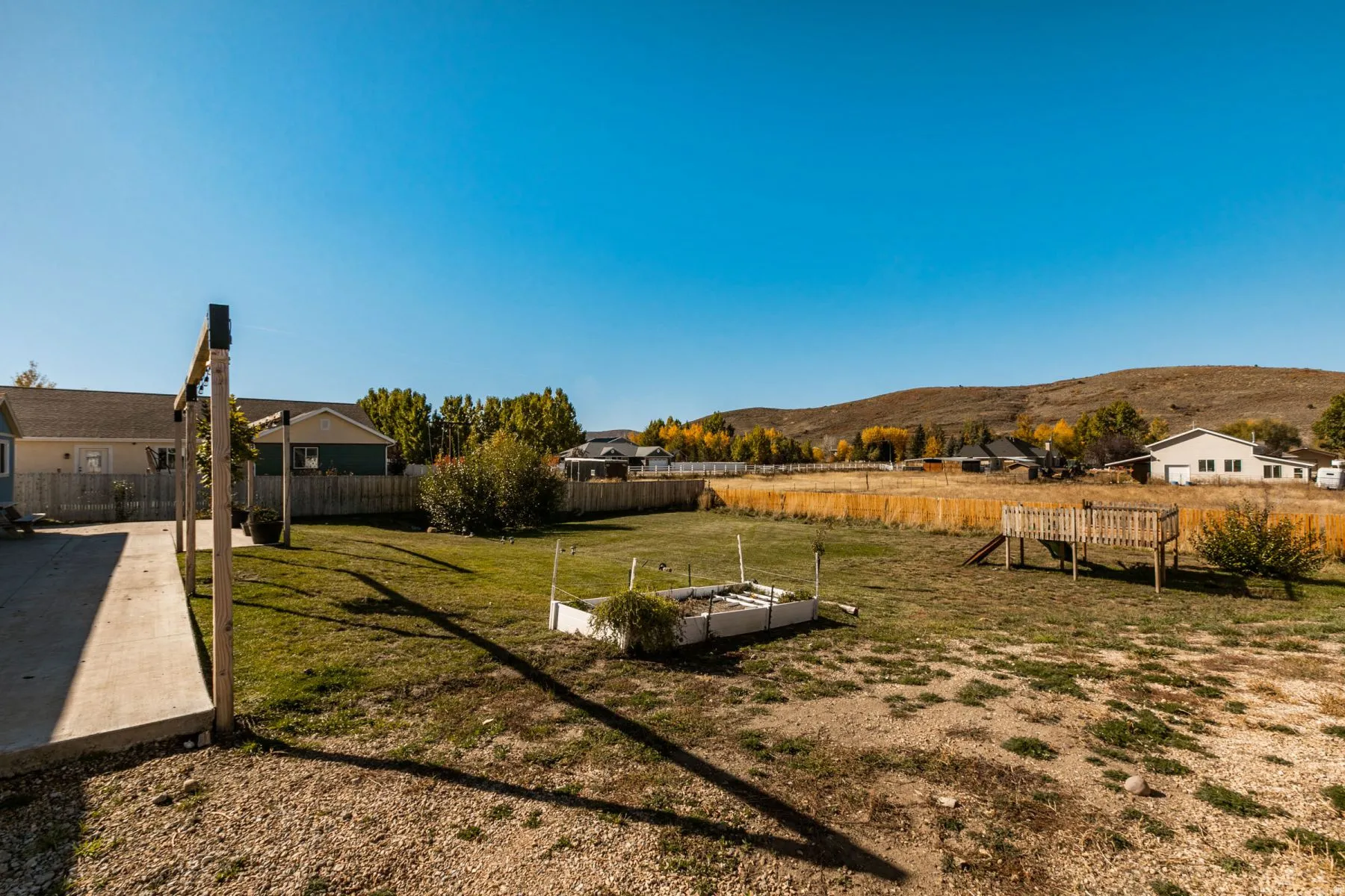 Expansive backyard featuring a combination of gravel and green lawn areas, a wooden play structure, and a raised garden bed
