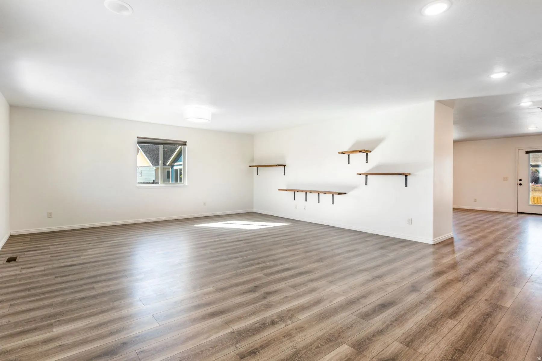 Spacious room featuring wood-finish flooring, white walls, recessed ceiling lighting, and a large window