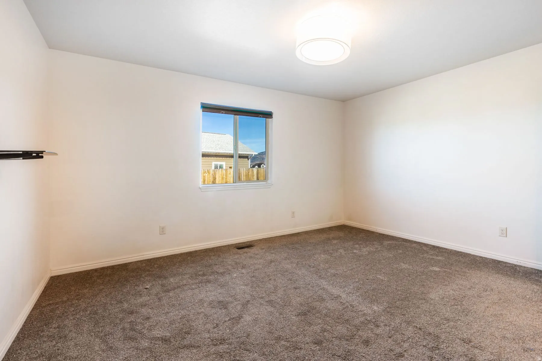 Neutral-toned room featuring a single window with dark trim, a flush-mount ceiling light, and gray carpeting