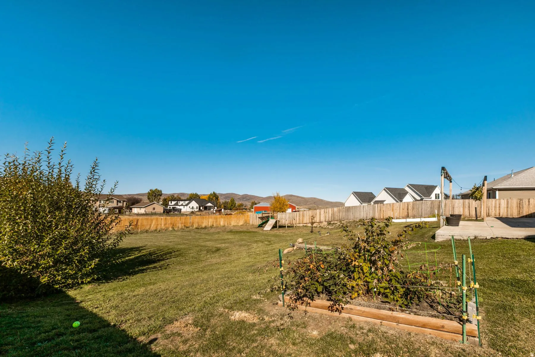 Expansive backyard featuring a manicured lawn, established garden beds, mature shrubbery, a concrete patio, and a wood privacy fence