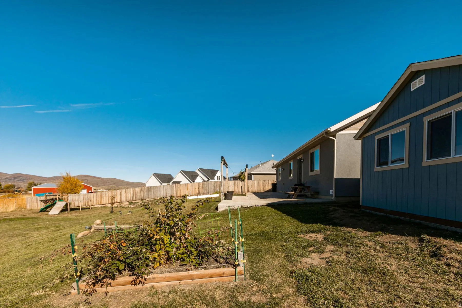 Expansive backyard featuring a privacy fence, concrete patio, and a raised garden bed