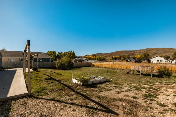 Expansive backyard featuring a combination of gravel and green lawn areas, a wooden play structure, and a raised garden bed