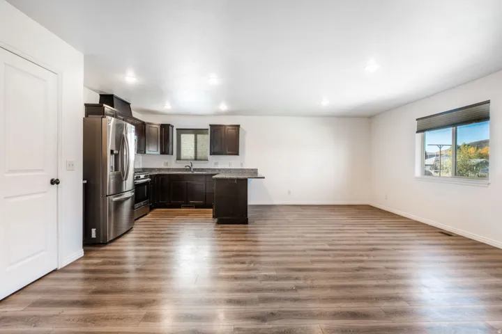 Open-concept living area with wood-finish flooring, recessed lighting, and a kitchen featuring dark cabinetry, stainless steel appliances, and a breakfast bar