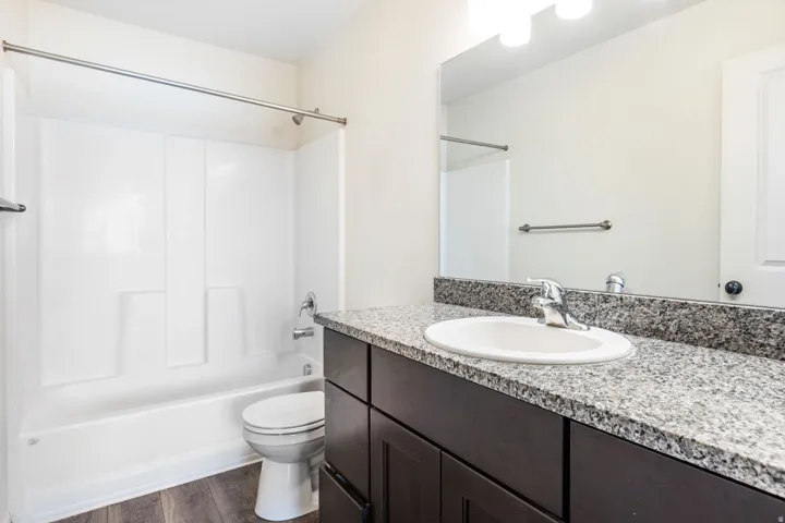Full bathroom featuring a dark wood-finish vanity with a light granite countertop, an undermount sink, and a chrome faucet