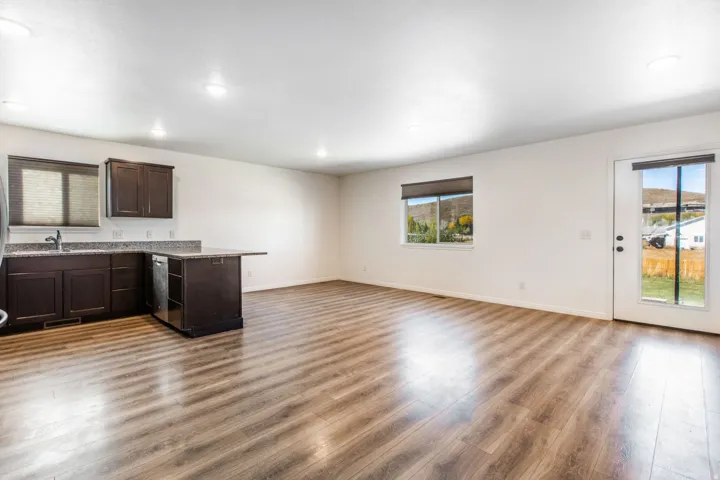 Open concept living area featuring wood-finish flooring, recessed lighting, and a modern kitchen with dark cabinetry and speckled countertops