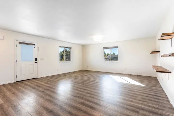 Spacious room featuring wood-finish flooring, white walls, and a white entry door with a frosted glass panel