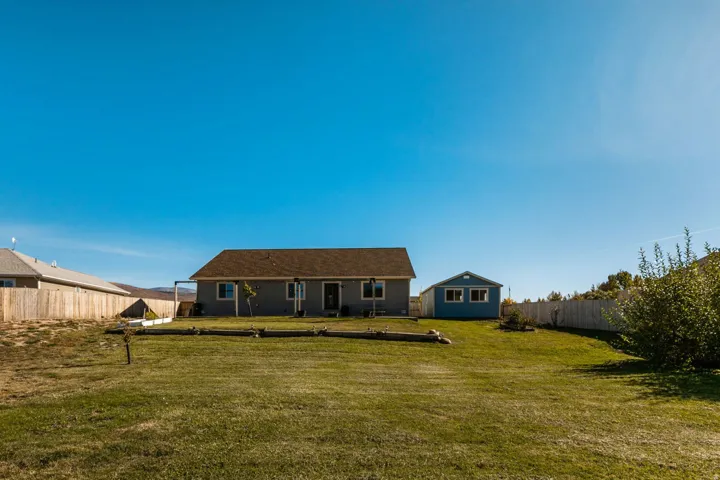 Expansive green lawn with a gray exterior residence, a detached blue utility building, and a wood privacy fence