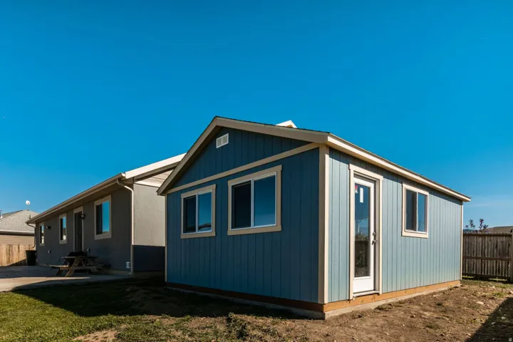 Detached accessory structure featuring blue vertical siding, multiple windows with light-colored trim, and a side entry door